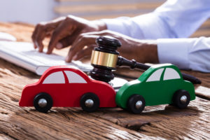 Two wooden toy cars getting in an accident with a gavel in the background